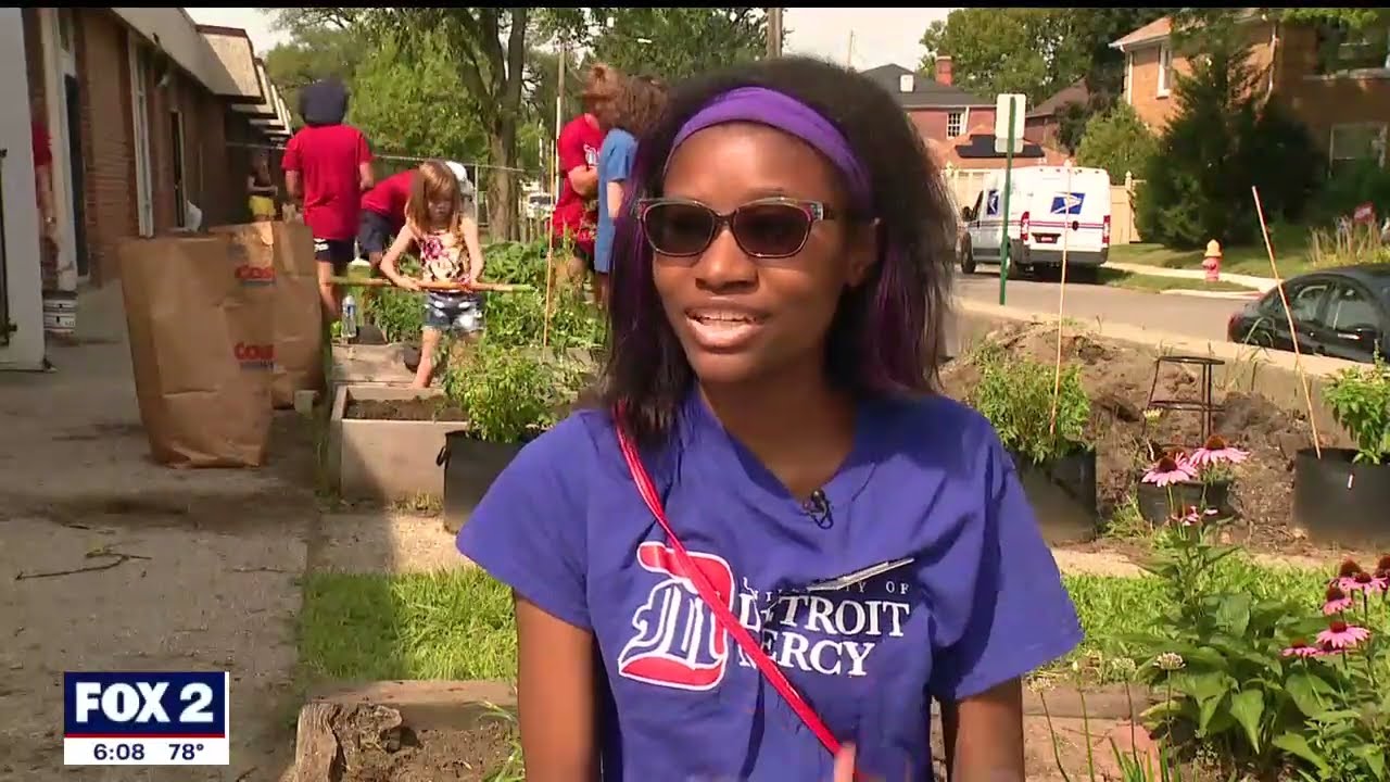 A Detroit Mercy student is interviewed during community service work outside of a school, with other people in the background.