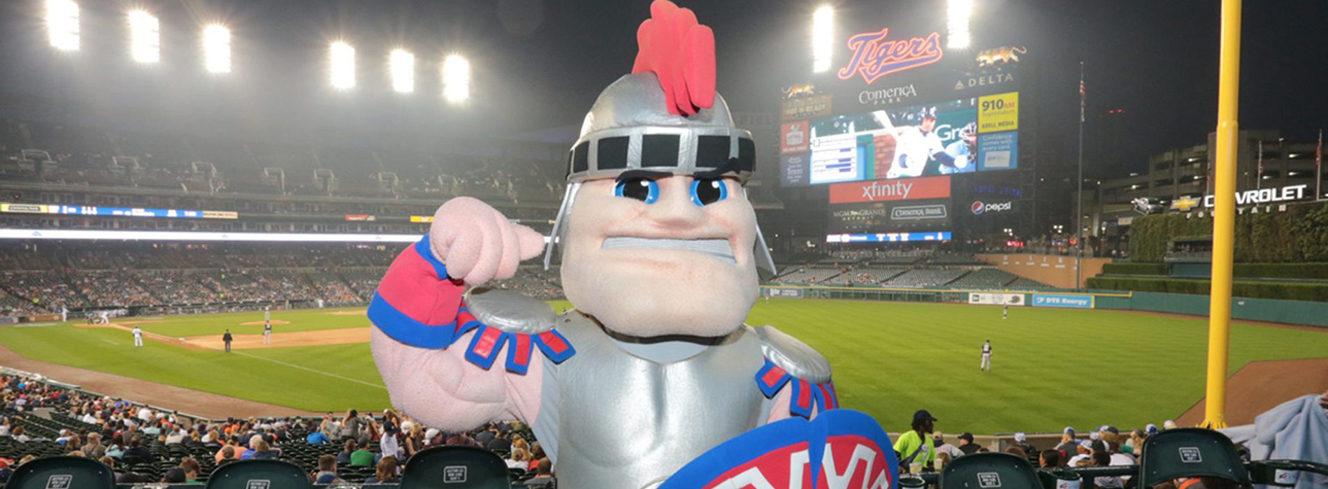 An image of Tommy Titan standing above the baseball field at Comerica park with the scoreboard in the background.