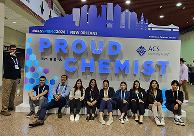 A group representing 太阳城娱乐城's Chemistry Club poses for a photo in front of a display for the ACS New Orleans 2024 conference. The display has text that reads 