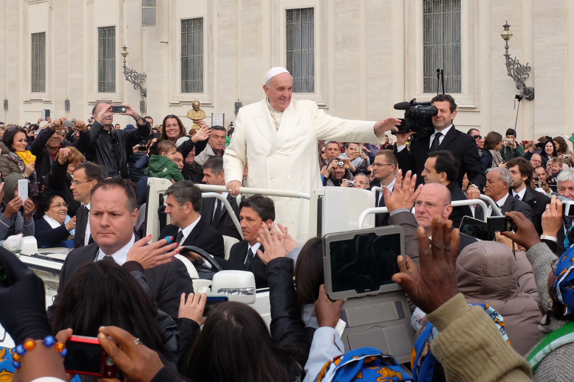 A image of Pope Francis in a small car, being driven through hundreds of people.