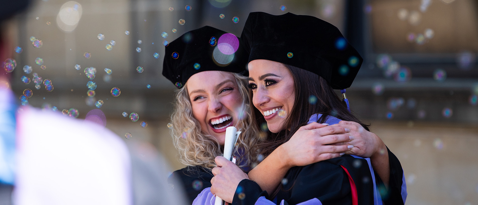 A pair of graduates smile as bubbles surround them.