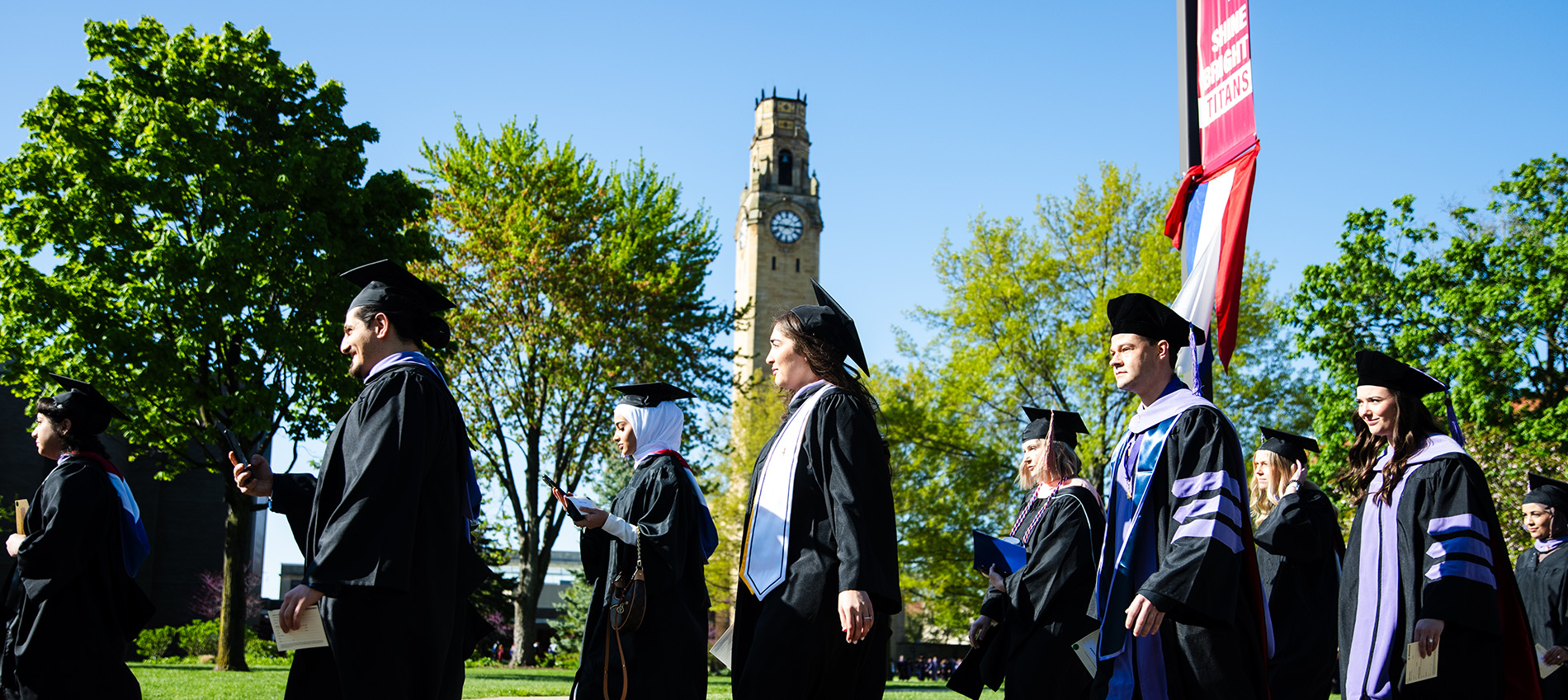 Graduates walk past the clocktower at the start of commencement.