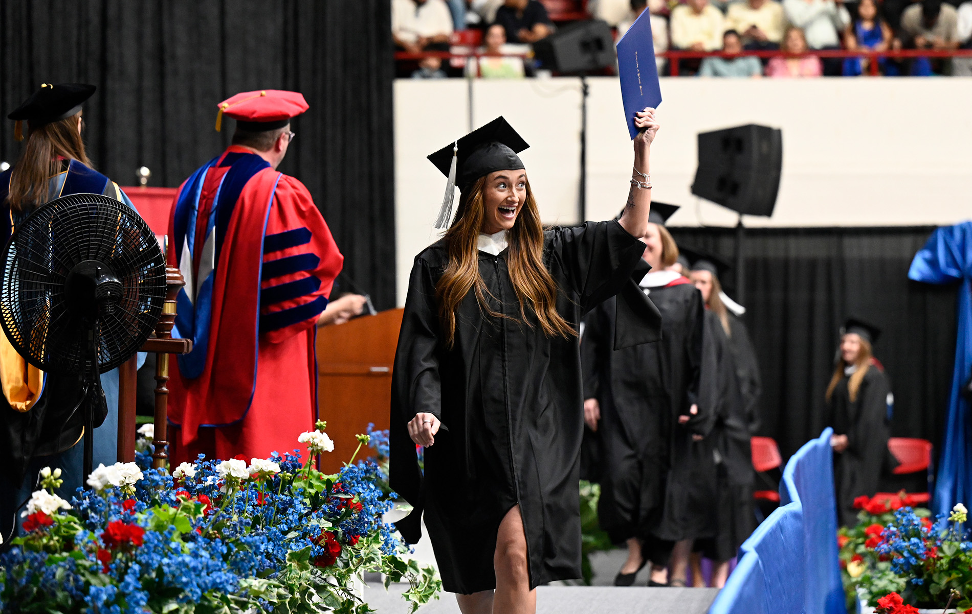 A graduate lifts her diploma up as she celebrates on the commencement stage.