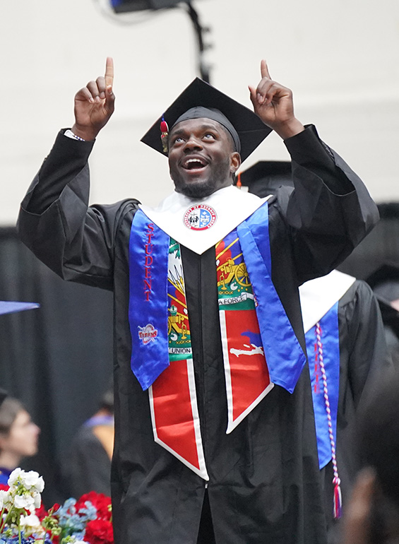 A graduate points to the sky during commencement