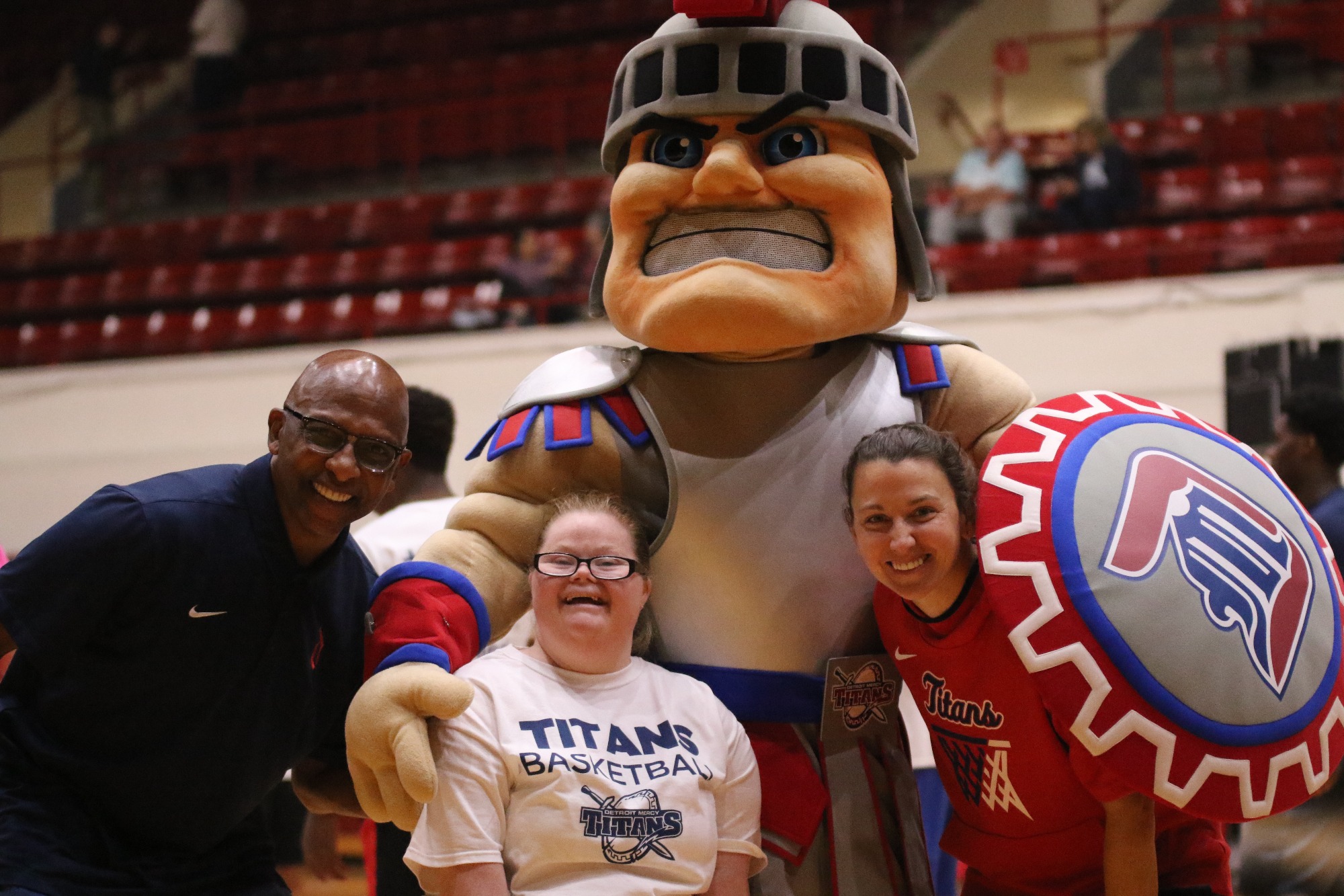 Three people stand inside of Calihan Hall with the 太阳城娱乐 mascot, Tommy Titan.