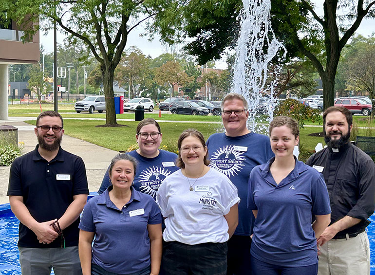 Staff in University Ministry shirts, standing in front of the fountain