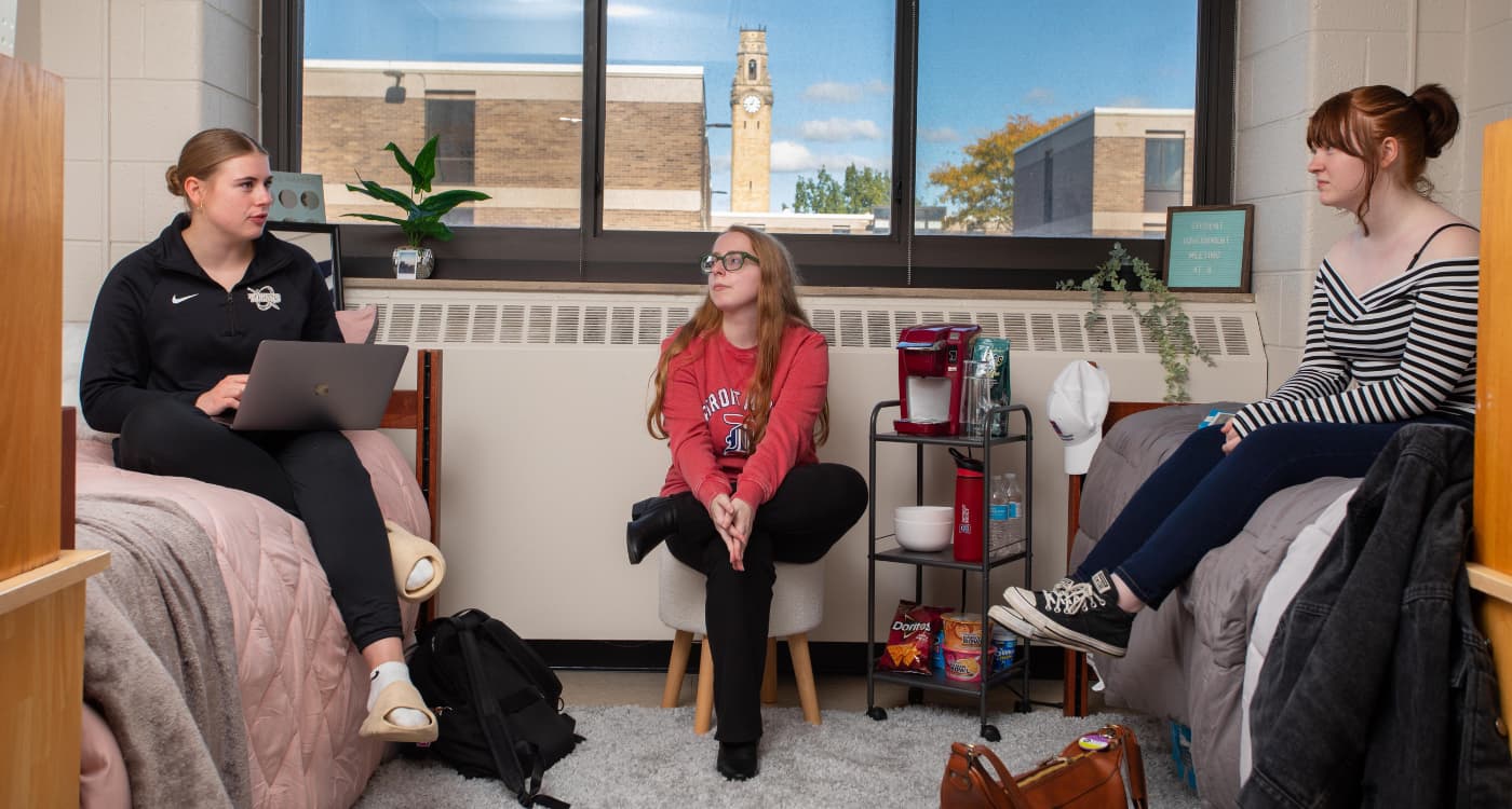 Three students sit in a dorm room in Shiple Hall.