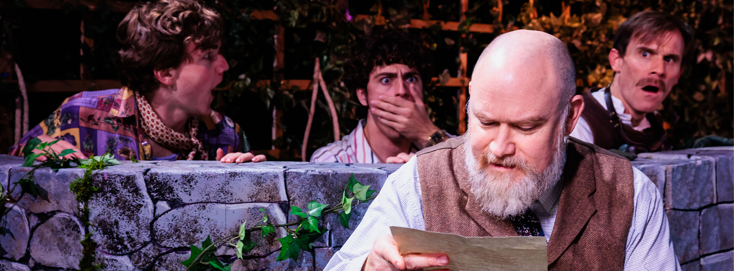 An actor reads a letter while three actors hide behind him